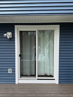 Sliding glass door with white trim on blue house siding and a small deck in front