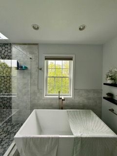 Modern bathroom with a freestanding tub, tiled shower, window, and black shelves