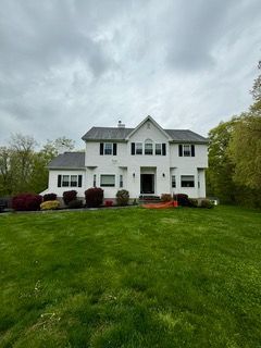 White two-story house with black shutters and a green lawn under an overcast sky