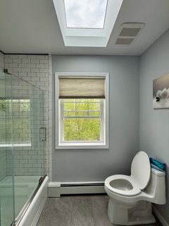 Modern bathroom with glass shower, window, skylight, and toilet