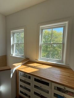 Bright room with two sunlit windows and a wooden countertop above cabinet drawers