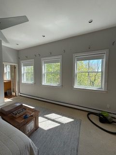 Bright living room with three windows, a vaulted ceiling, and sunlight on a beige carpet.