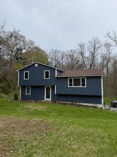 Blue two-story house with white trim on a grassy lot under an overcast sky