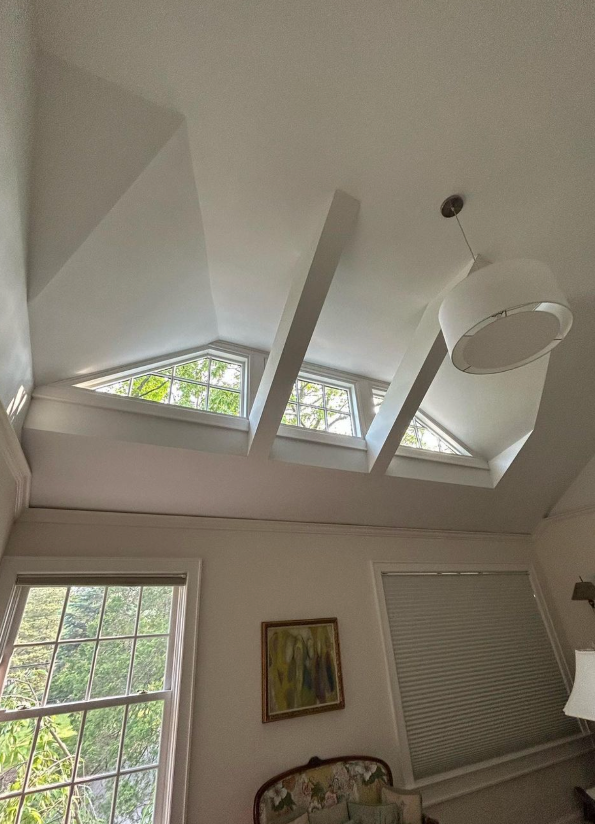 Interior room with high angled ceiling, triangular windows, beams, and a hanging light.
