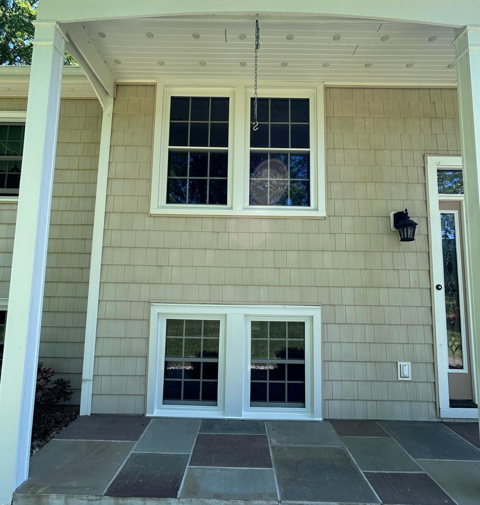 Exterior of a house with two sets of windows and a covered porch; stone patio.