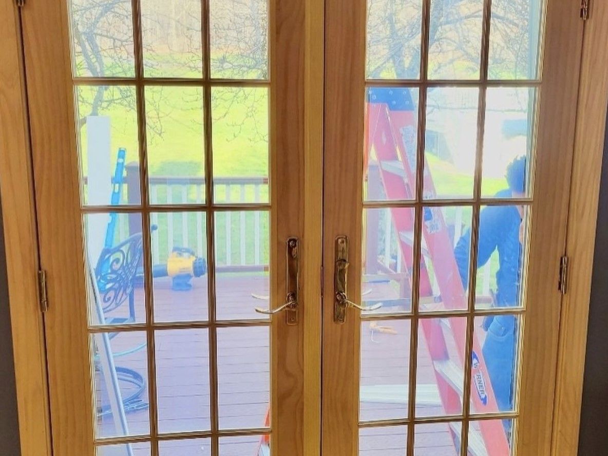 Wooden French doors with multiple panes, view to a deck and yard, ladder propped up.