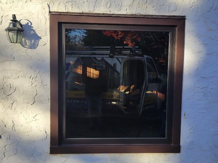 Brown framed window reflecting a van, trees, and a house on a stucco wall. A lamp hangs to the left.
