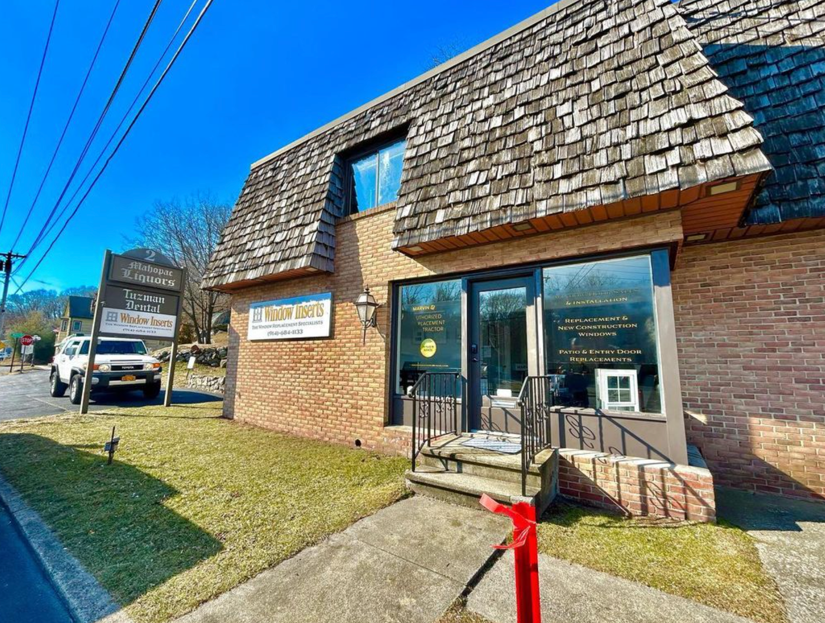 Building with brown brick, cedar shingle roof. "Le Vintage" sign above door. Small sign on the left reads "The Stone Cottage".