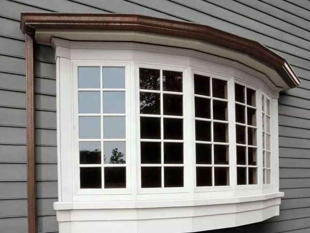 Bay window with white frame, on a gray house, with a brown roof.