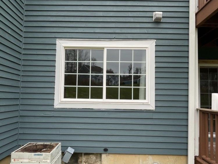 Exterior view of a blue-sided house with a white-framed window. A/C unit sits below.