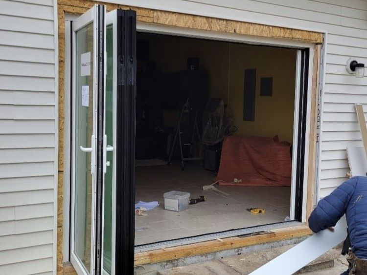 Exterior view of a partially open white and black folding door being installed. A person works on the trim.