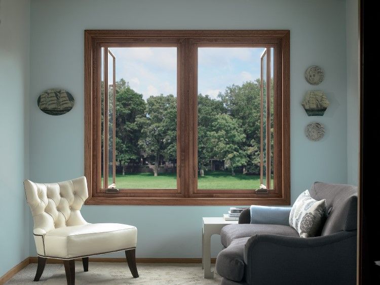 Room with open window, overlooking trees. Light blue walls, wood trim, white chair, and gray couch.