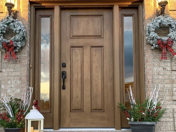 Wooden front door with sidelights, decorated with wreaths and holiday plants.