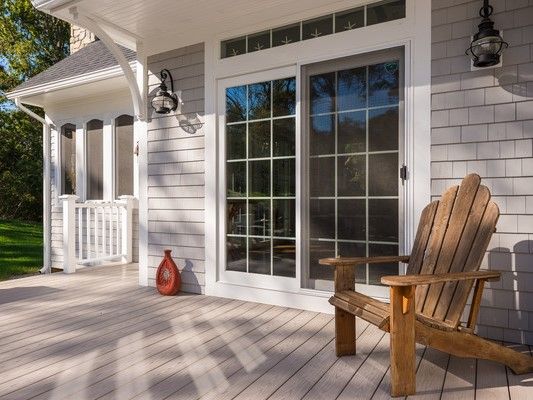 Wooden chair on a porch next to a sliding glass door. Gray siding, red vase, outdoor lights.