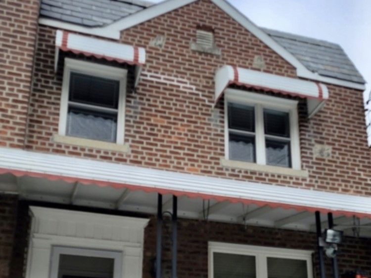 Two-story brick building with white window awnings trimmed in red. Gray roof.