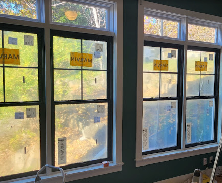 Three new windows with black frames and white trim; green wall, outside view of trees.