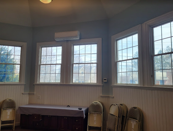 Room with windows, blue walls, white wainscoting, an air conditioner, and folding chairs.