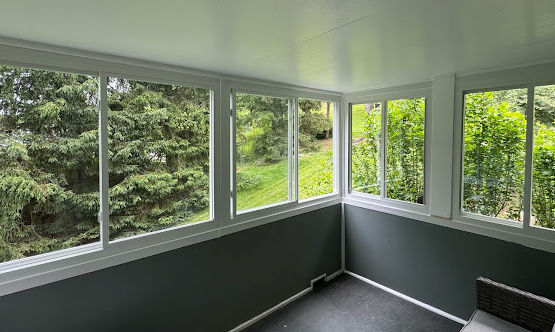Sunroom with multiple windows overlooking lush greenery and a dark gray floor.