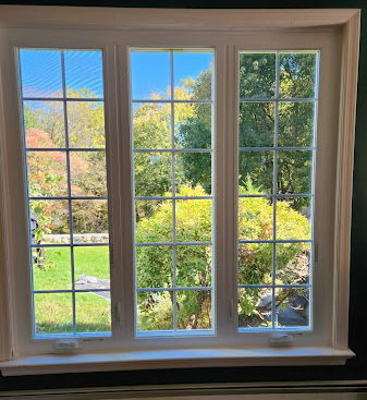 Three-paneled window with white grids, showing a bright, colorful outdoor scene with trees and sky.