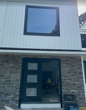 Modern house exterior with dark trim and a large square window above a black door.