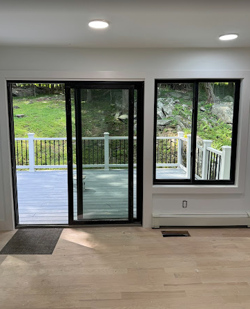 Interior view of a room with a sliding glass door and window looking out to a deck. Light-colored flooring and white walls.