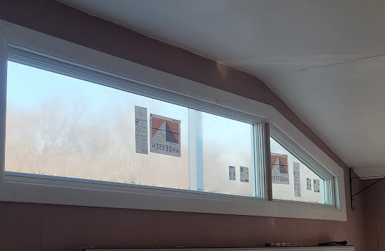 Angled white-framed window. Exterior visible through frosted glass. Light pink wall, white ceiling.