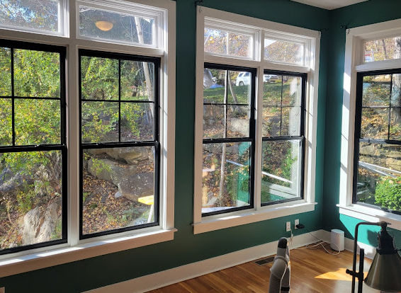 Interior corner room with dark-framed windows, white trim, and green walls. The windows overlook a tree-filled outdoor space.