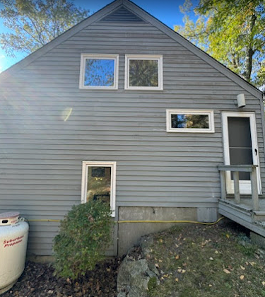 Gray house exterior with windows, door, and propane tank. Bush in front.