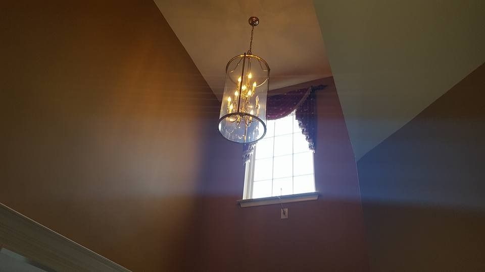 Tall room with a hanging chandelier, a window with curtains, and tan walls.