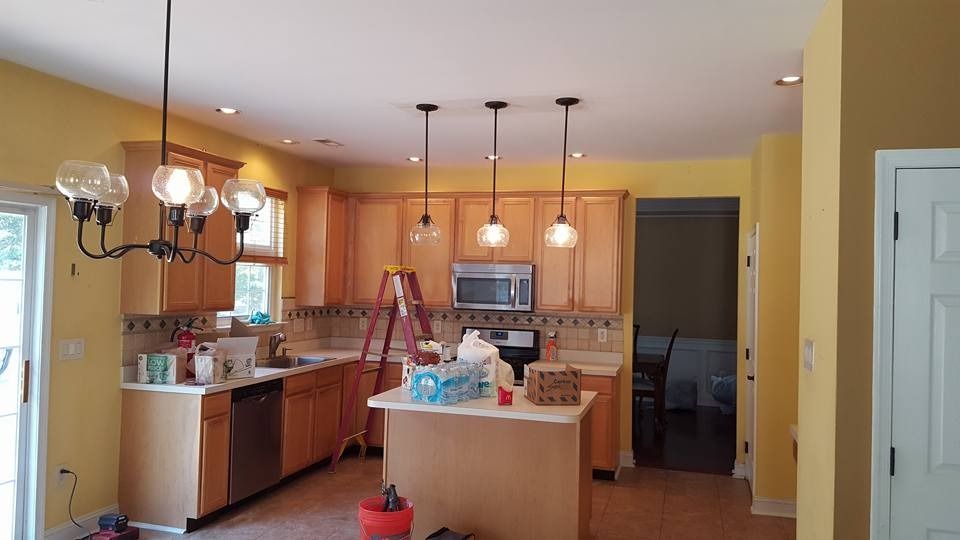Kitchen with wooden cabinets, island, three pendant lights, yellow walls, and a white ceiling.