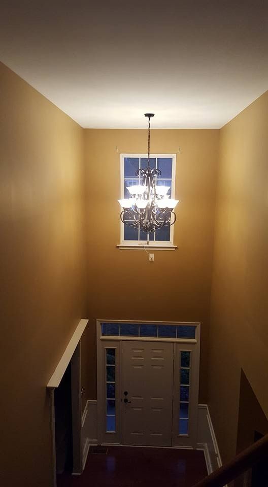 High-ceiling entryway with a chandelier over a door and a window above. Tan walls and dark wood floor.