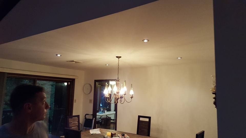 A person looks toward a lit chandelier, recessed ceiling lights, and dining area with a sliding glass door.