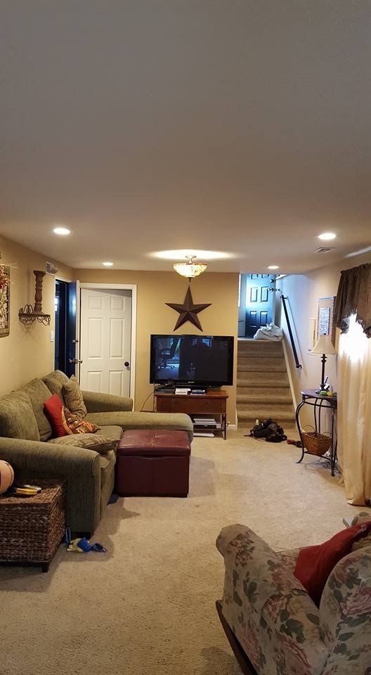 Cozy living room with sectional sofa, TV, and staircase leading upwards. Neutral color palette with warm lighting.