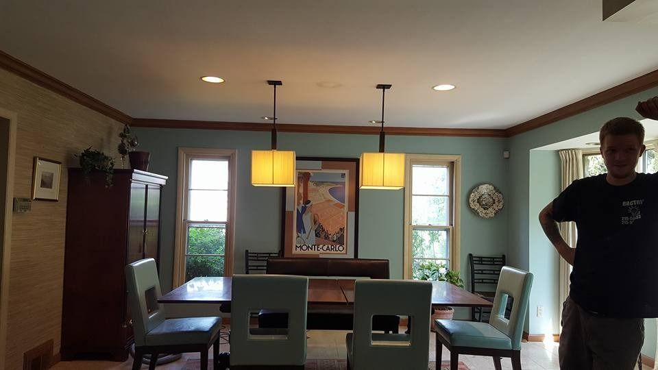 Dining room with table, chairs, art, windows, light fixtures, and a person.