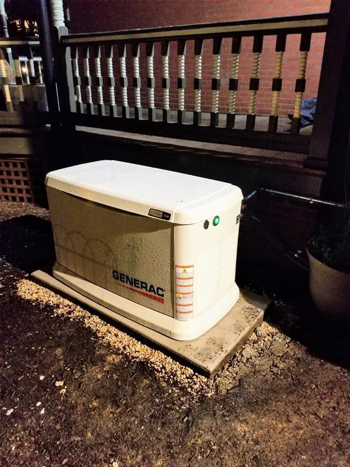 A white and tan Generac generator sits on a concrete pad outside a house at night.