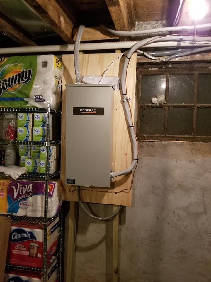 Electrical panel mounted on wood in a basement, with conduits running to it.