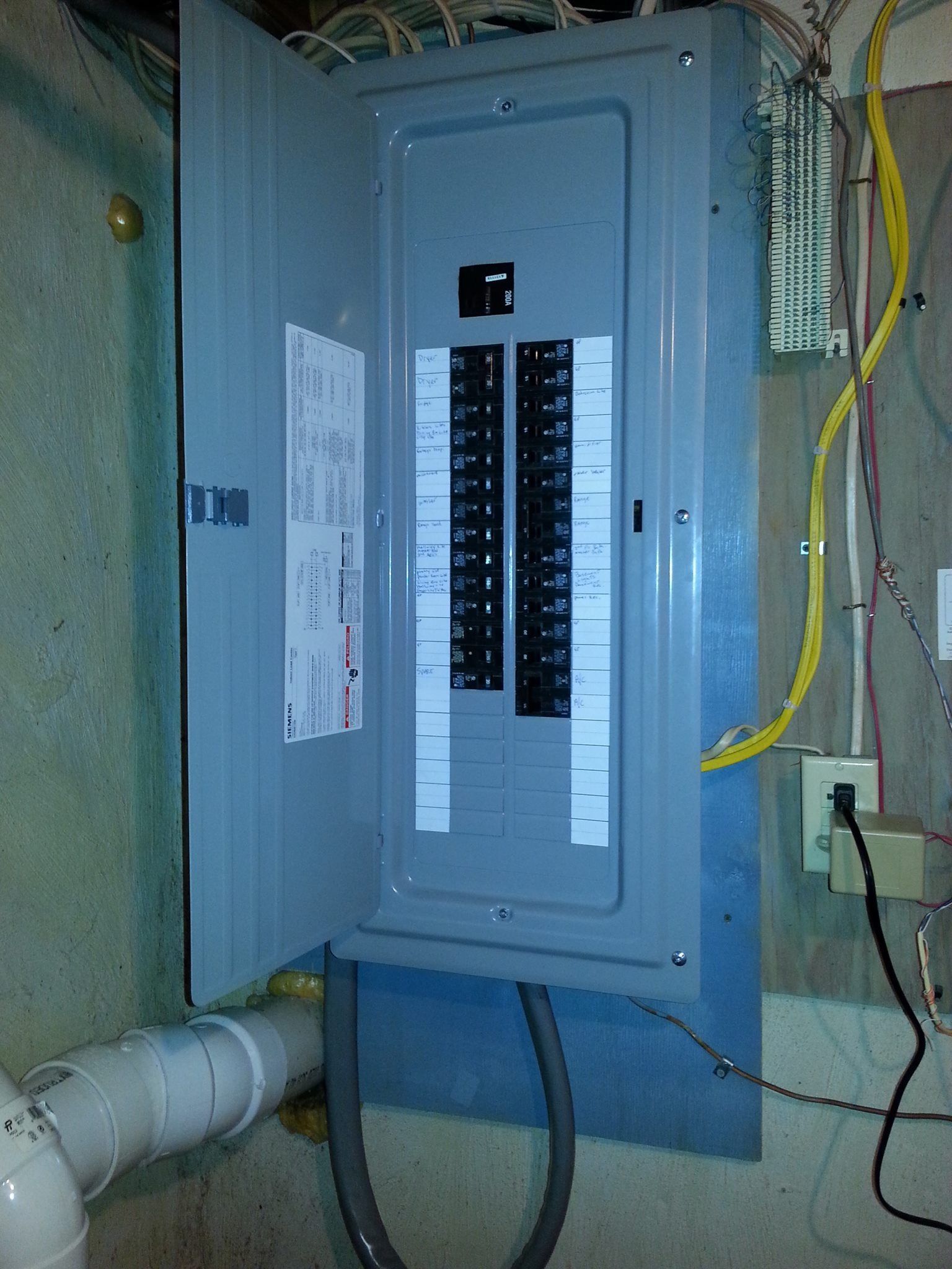 Opened gray electrical panel with circuit breakers. Cables and conduit are visible.