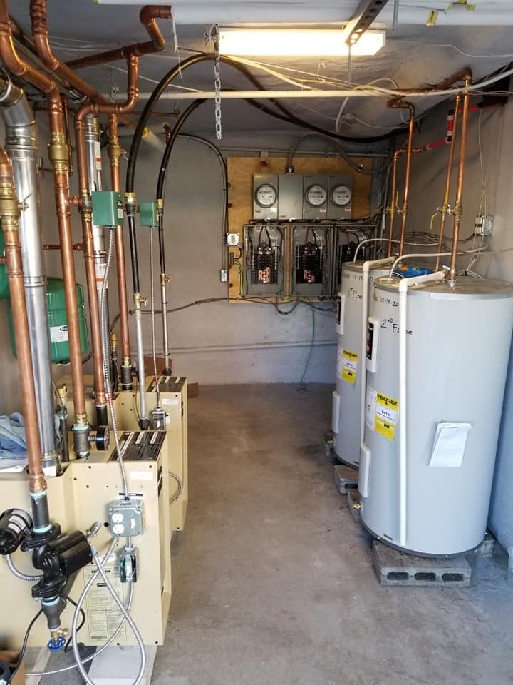 Utility room with water heaters, electrical panels, copper pipes, and a boiler.