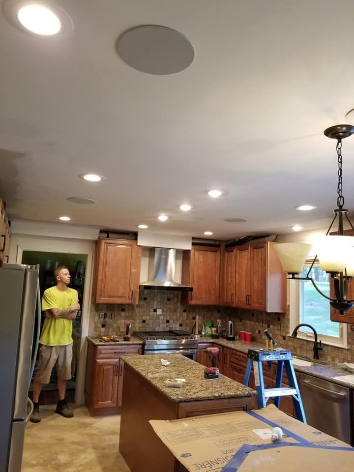 Man in kitchen with installed ceiling lights, speaker, and cabinets.