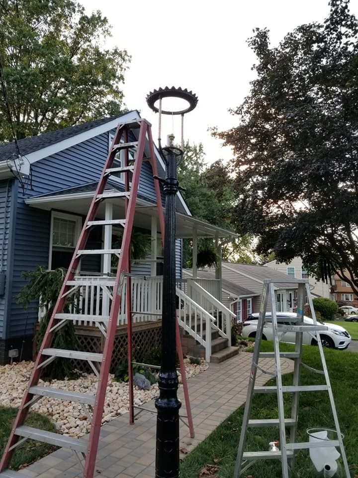 Two ladders next to a black lamp post in front of a blue house and porch.