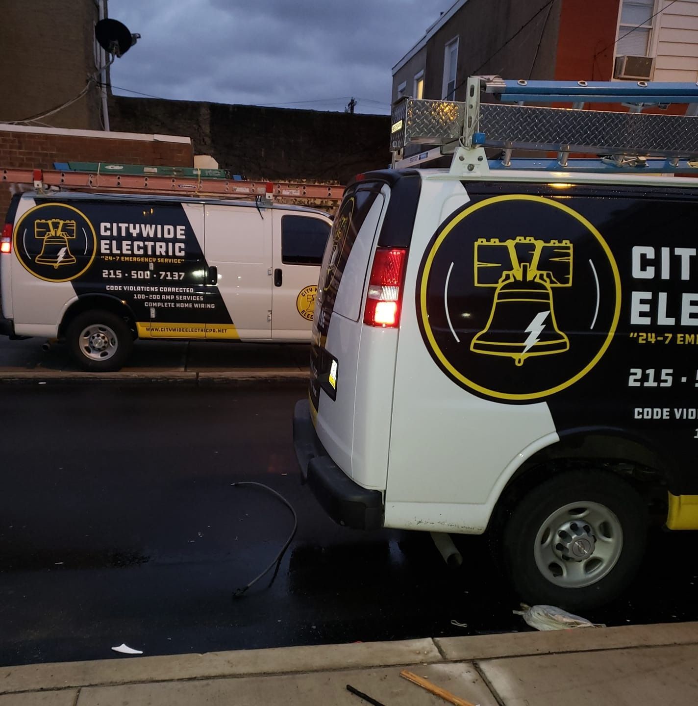 Two white Citywide Electric vans parked on a city street. Each has a Liberty Bell logo.