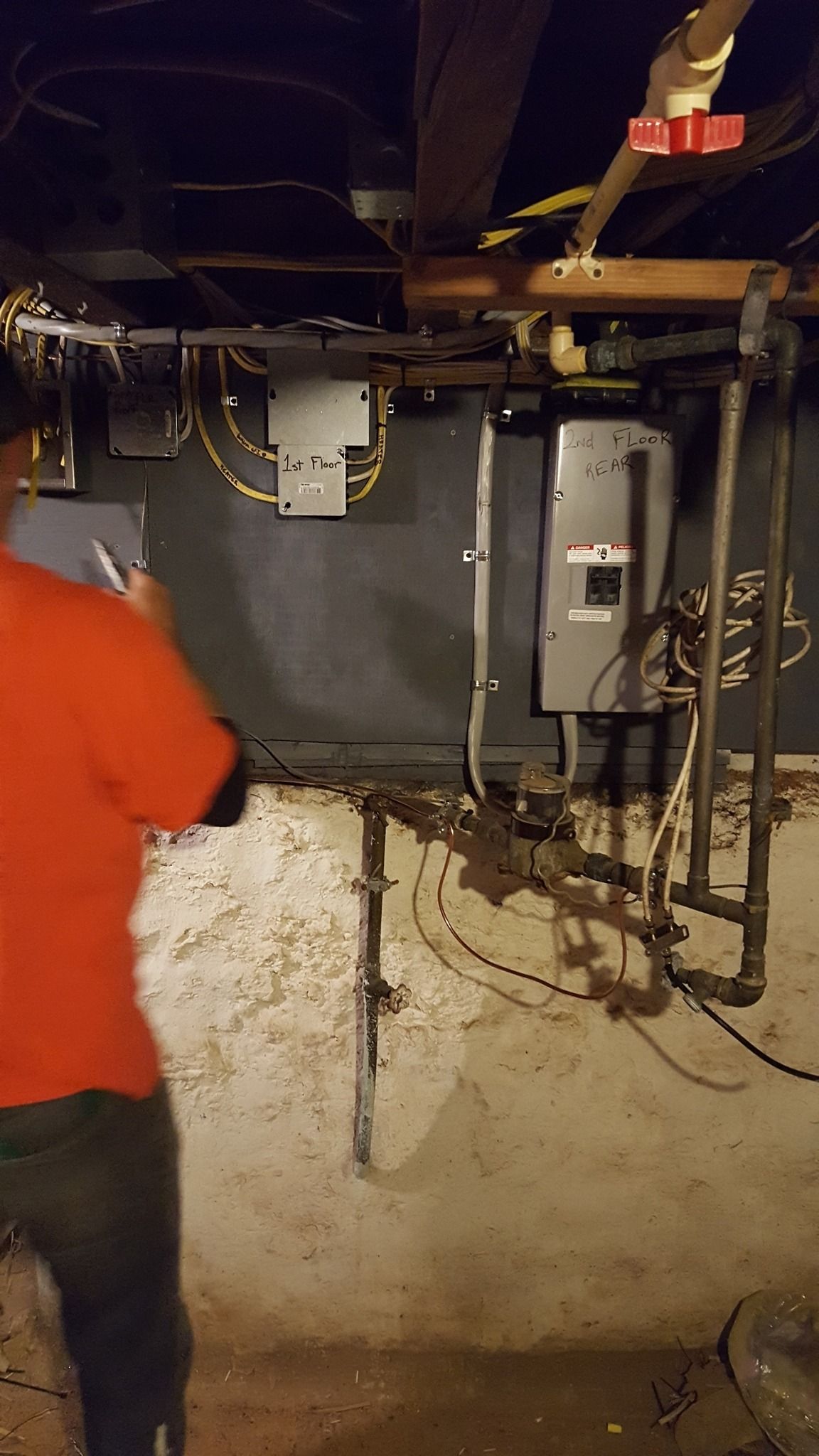 Person in red shirt by electrical equipment in a basement.