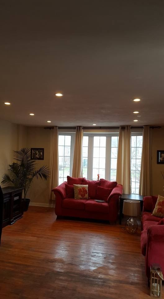 Living room with red couches, hardwood floor, window with beige curtains, and recessed lighting.