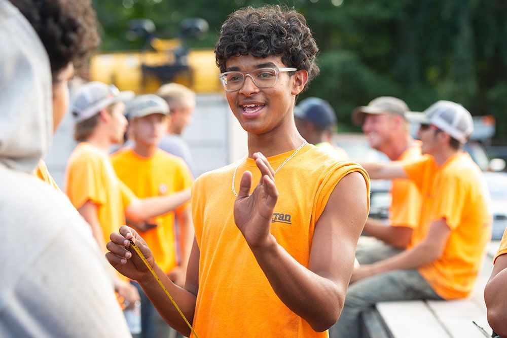 One of the Curran Corp Landscape & Excavation team members in an orange shirt is smiling and gesturing while standing with a group outdoors.