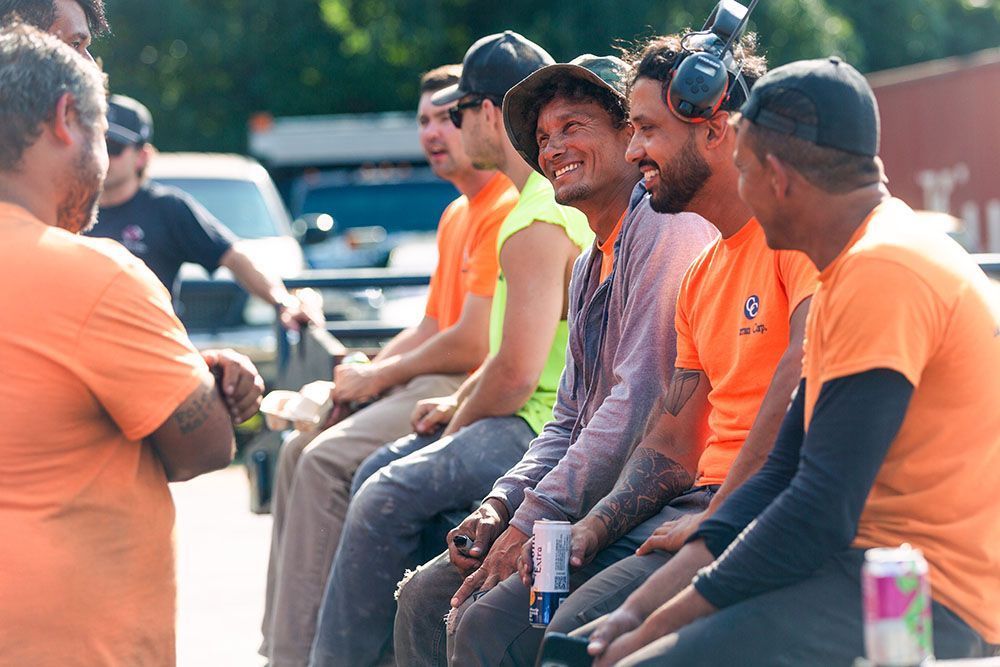 Professionals from the excavation team at Curran Corp Landscape & Excavation in orange shirts are sitting together outdoors.