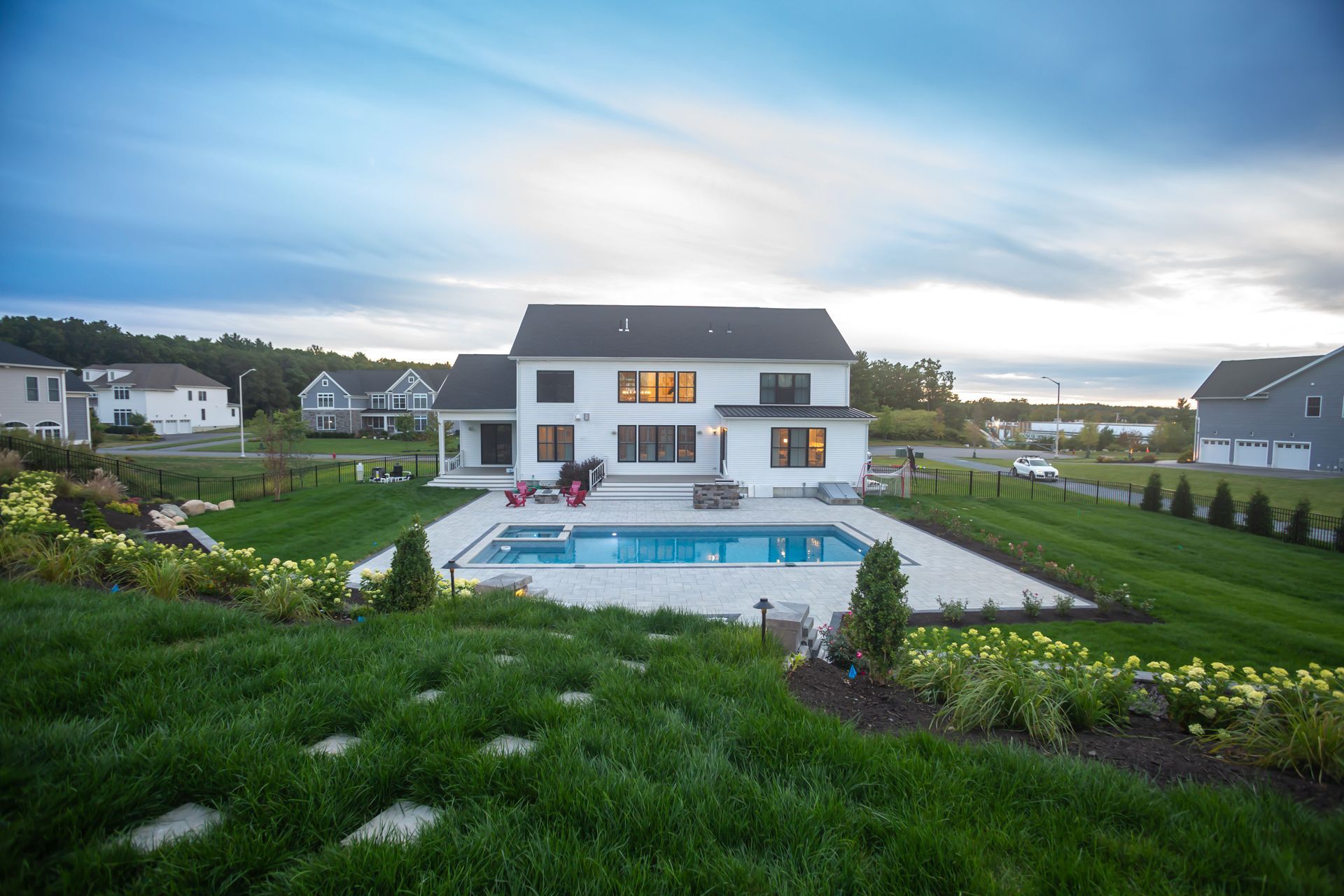 Modern house with lit windows, backyard pool, and green lawn at dusk by the waterfront