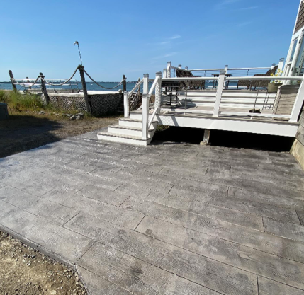 Gray stamped concrete patio with wooden deck and ocean view.