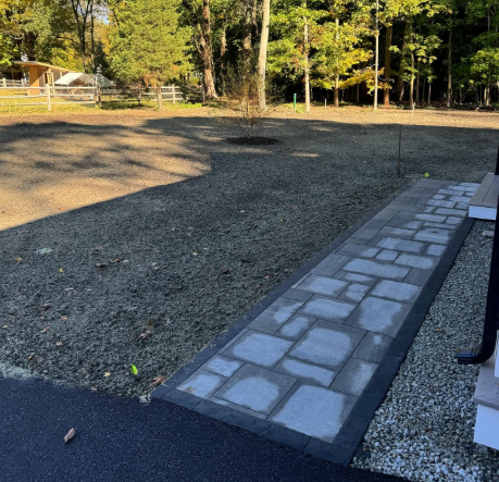 Stone walkway leading from dark pavement to gravel yard with trees.