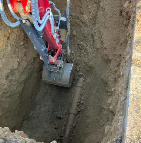 Mini excavator digging in a trench, next to a buried pipe.