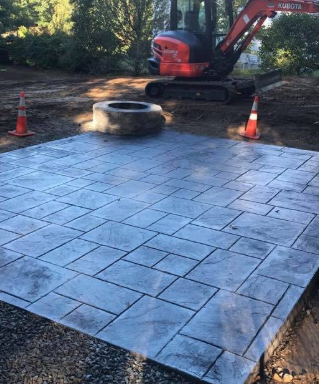 A freshly poured, patterned concrete patio with a fire pit, construction equipment visible in the background.